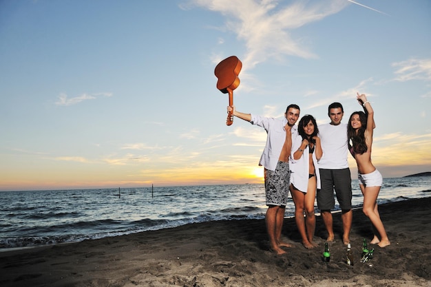 Fröhliche junge Freundesgruppe hat Spaß und feiert beim Springen und Laufen am Strand bei Sonnenuntergang