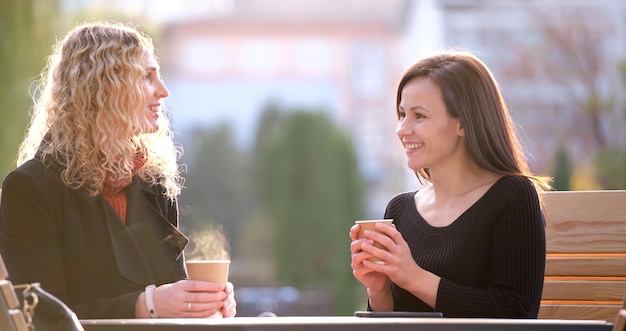 Fröhliche junge Freundinnen, die während der Arbeitspause im City Street Restaurant Kaffee trinken Geselligkeit und Freundschaftskonzept