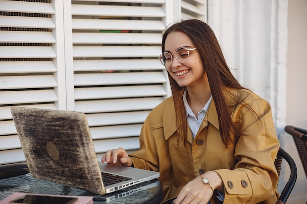 Fröhliche junge Geschäftsfrau, die einen Laptop benutzt und aus der Ferne im Straßencafé an einem Online-Projekt arbeitet