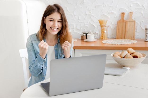 Fröhliche junge Geschäftsfrau freut sich über ihre Arbeitsleistung und lächelt auf den Laptop
