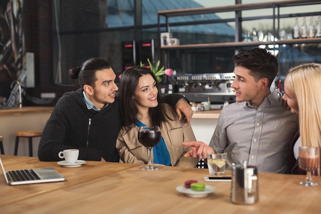 Fröhliche junge Gesellschaft von Freunden, die Kaffee trinken und reden, während sie in einem modernen Café sitzen, Platz kopieren.