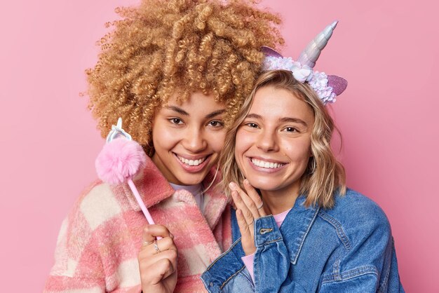 Fröhliche junge hübsche Frauen lächeln fröhlich, haben gute Laune, äußern positive Emotionen, posieren zusammen, um Fotos zu machen, die in modischen Jacken gekleidet sind, die über rosafarbenem Hintergrund isoliert sind Beste weibliche Freunde