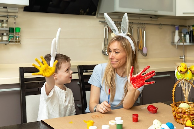 Fröhliche junge Mutter und ihr kleiner Sohn haben Spaß und malen auf ihren Händen Osterfamilientraditionen