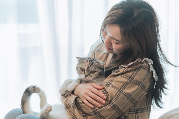 Fröhliche junge schöne asiatische Frau, die zu Hause Katze im Bett umarmt