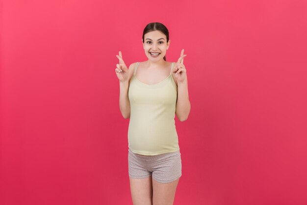 Fröhliche junge schwangere Frau, die die Daumen hält und auf Schwangerschaft isoliert auf farbigem Hintergrund im Studio-Lifestyle-Schwangerschaftskonzept wartet