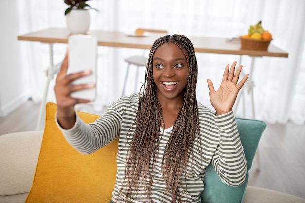 Fröhliche junge schwarze Dame, die mit Freundin online über Smartphone spricht