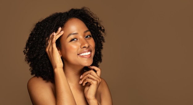 Fröhliche junge schwarze Frau posiert oben ohne auf braunem Hintergrundpanorama