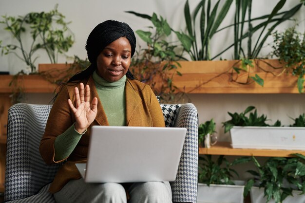 Fröhliche junge schwarze Frau winkt dem Patienten während der Online-Sitzung mit der Hand