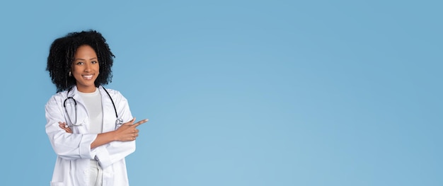 Fröhliche junge schwarze Ärztin und Therapeutin im weißen Kittel zeigt mit dem Finger auf den Kopierraum