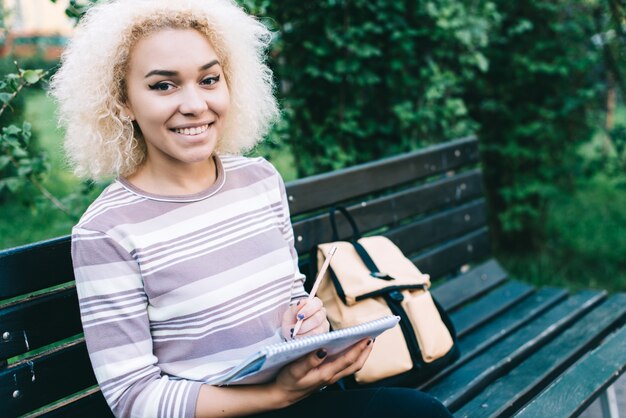 Fröhliche junge Student Mädchen im Freien sitzt auf der Bank