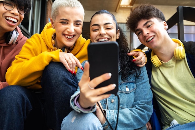 Fröhliche junge Studentenfreunde schauen sich das Handy an und lachen zusammen Social-Media-Sucht