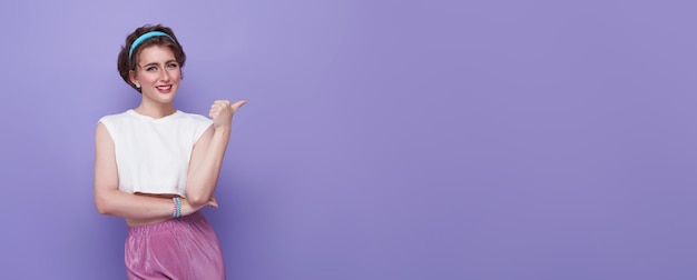 Fröhliche junge teenager-frau, die mit ihrem finger zeigt, isoliert auf lila hintergrund mit kopier-spa