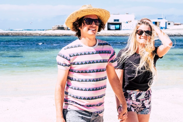 Fröhliche junge Touristen haben Spaß und genießen einen sonnigen Tag am Strand Paar lächelt und geht Händchen haltend in den Sommerferien mit blauem Ozean im Hintergrund Reisen Sie den Lebensstil der Menschen