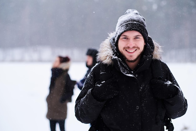 Fröhliche junge Wanderin, die in einem Kamerastand neben ihren Freunden im verschneiten Wald posiert