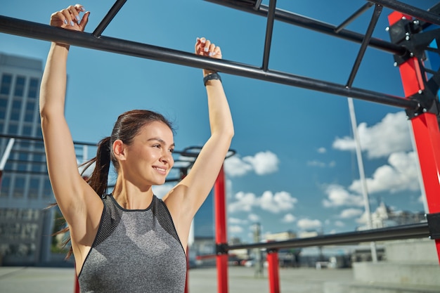 Fröhliche junge weibliche Person, die beim Sport ein Lächeln auf dem Gesicht hält