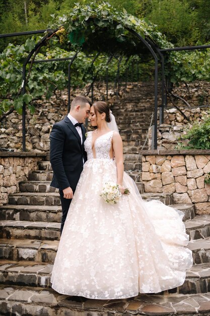 Fröhliche Jungvermählten spazieren gemeinsam durch den großen Park, ein hübscher Bräutigam und eine elegante Braut bei ihrer Hochzeit