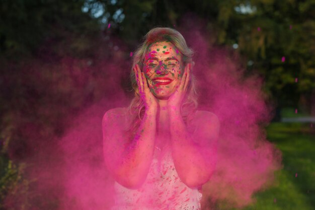 Fröhliche kaukasische Frau mit lockigem Haar, die eine Wolke aus rosafarbener trockener Farbe steht und das Holi-Festival feiert