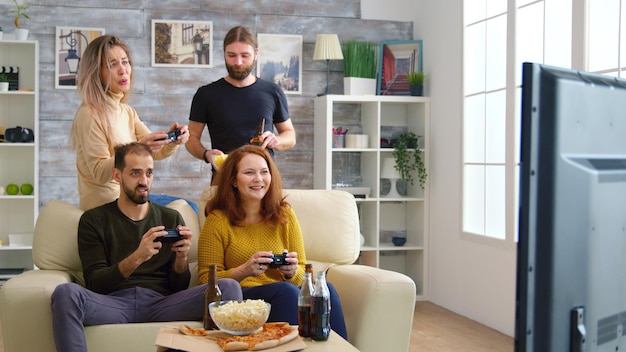 Fröhliche kaukasische Freunde, die Videospiele auf dem großen Fernseher im Wohnzimmer spielen.