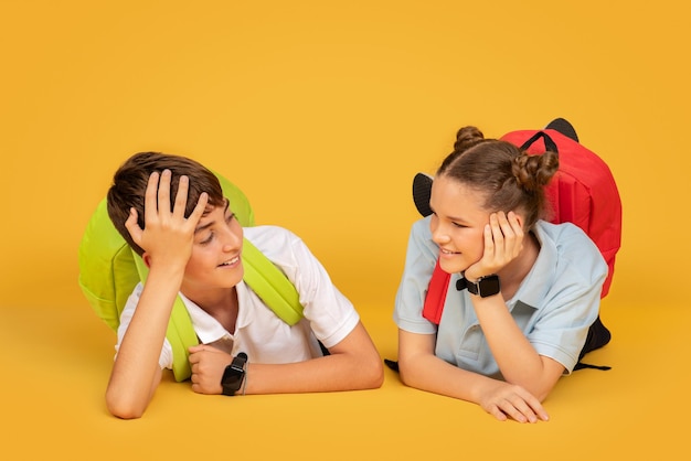 Fröhliche kaukasische Teenager-Mädchen und -Jungen mit Rucksäcken liegen auf dem Boden und kommunizieren