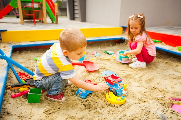 Fröhliche Kinder, die draußen auf dem modernen Spielplatz mit Sand spielen.