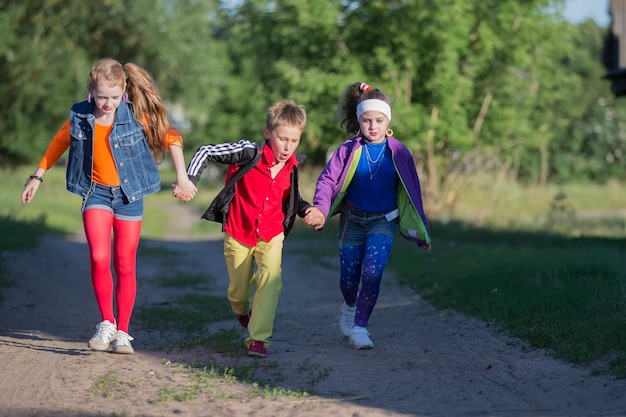 Fröhliche Kinder, ein Junge und zwei Mädchen in coolen Outfits, laufen die Straße entlang