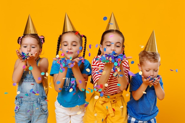 Foto fröhliche kinder im urlaub haben spaß und springen in bunten konfetti auf gelbem hintergrund