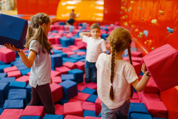 Fröhliche Kinder spielen im Unterhaltungszentrum zwischen weichen Würfeln. Freizeit für Mädchen und Jungen im Urlaub, Kinderglück, glückliche Kinder auf dem Spielplatz