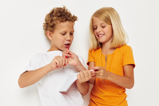 Fröhliche Kinder stehen neben einem Notizblock mit Bleistift, der Emotionen unverändert auf farbigem Hintergrund zeichnet