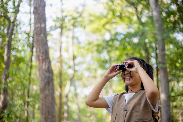 Fröhliche kleine asiatische Mädchen blicken nach vorn und lächelndes Kind mit dem Fernglas im Park Reise- und Abenteuerkonzept Freiheitsurlaub