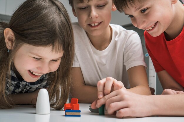 Fröhliche kleine Schulkinder spielen Spielzeug-Mini-Möbel auf dem Tisch in der Nähe Porträt von Kindern, die kleine Plastikdetails halten