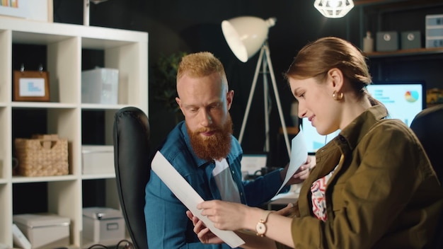 Fröhliche Kollegen diskutieren Ideen im Coworking Space. Erstaunter Geschäftsmann erzählt lächelndem Mädchen im Büro gute Nachrichten. Positives Geschäftspaar prüft Dokumente in stilvollem Interieur