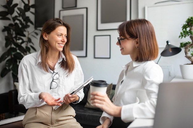 Fröhliche Kolleginnen genießen die Kaffeepause, zwei Geschäftsfrauen unterhalten sich, treffen sich und unterhalten sich