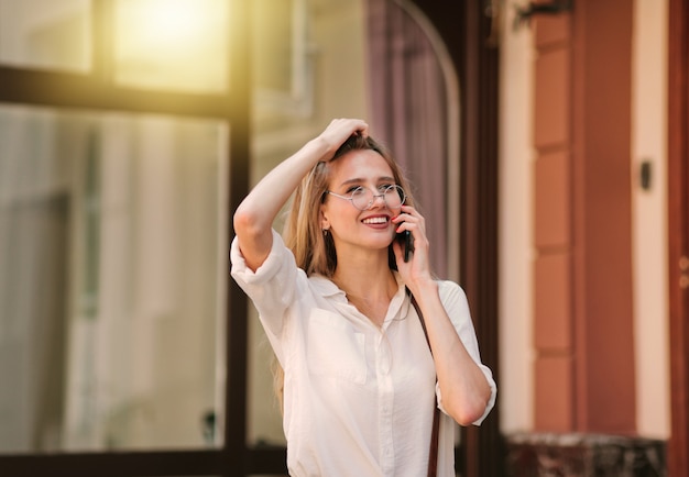 Fröhliche lächelnde blonde Frau, die draußen am Telefon spricht