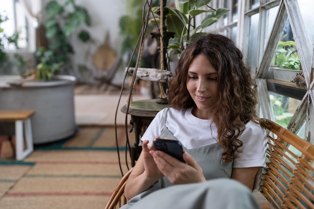 Fröhliche lächelnde Frau entspannt sich im heimischen Garten mit Smartphone-Chats in sozialen Medien mit Freunden