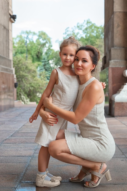 Fröhliche lächelnde Mutter mit einem Tochterkind an einem sonnigen Sommertag Mutter und Mädchen, die im Bogen durch die Stadt laufen