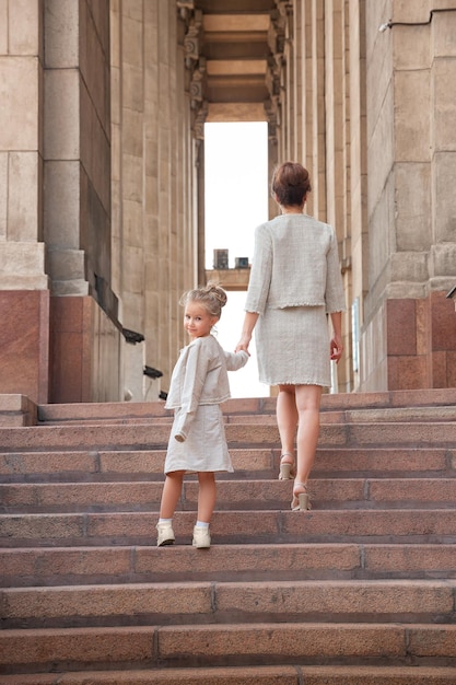 Fröhliche lächelnde Mutter mit einem Tochterkind an einem sonnigen Sommertag Mutter und Mädchen, die im Bogen durch die Stadt laufen