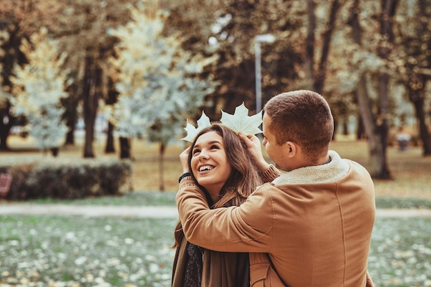 Fröhliche lächelnde romantische Menschen haben Spaß mit Ahornblättern im Herbstpark.