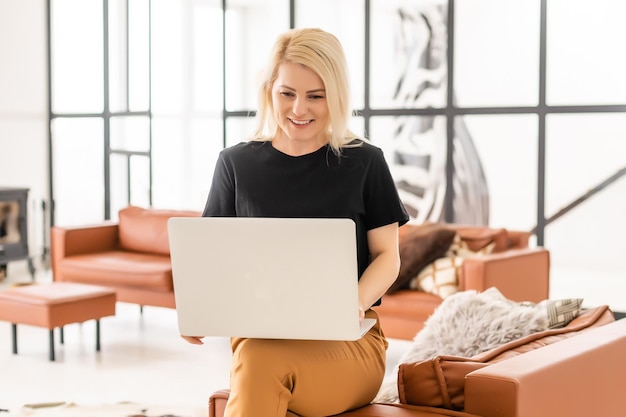 Fröhliche, lässige, schöne Frau, die an einem Laptop arbeitet, der im Haus sitzt.