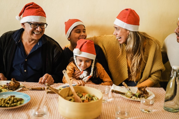 Fröhliche lateinamerikanische Familie, die während der Weihnachtszeit Spaß beim gemeinsamen Essen hat - Fokus auf Großvatergesicht