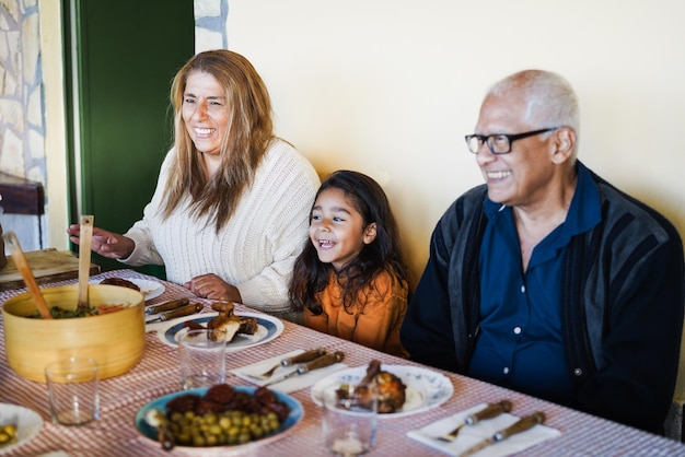 Fröhliche lateinamerikanische Großeltern haben Spaß beim Essen mit ihrer Enkelin zu Hause - Konzentrieren Sie sich auf das Gesicht der Großmutter