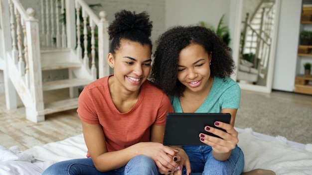 Fröhliche Mädchen unterhalten sich mit ihren Freunden zu Hause über einen Online-Video-Chat auf dem Tablet-Computer