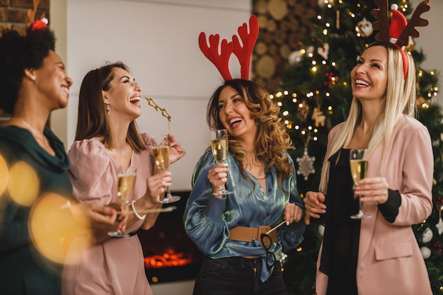 Fröhliche multiethnische Mädchen, die Spaß haben, während sie gemeinsam mit Champagner auf der Weihnachts- oder Neujahrsparty anstoßen.