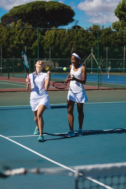 Foto fröhliche, multirassische tennisspielerinnen unterhalten sich, während sie an einem sonnigen tag auf dem platz spazieren gehen