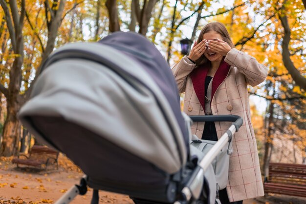 Fröhliche Mutter, die mit neugeborenem Baby im Kinderwagen spielt