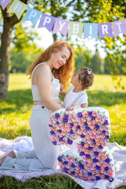 Fröhliche Mutter und Tochter, die sich am Kindergeburtstag auf einer Decke mit Papierdekorationen im Park amüsieren