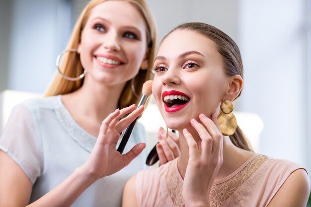 Fröhliche nette Frau, die ihre Wange berührt, während sie sich über ihr Make-up freut