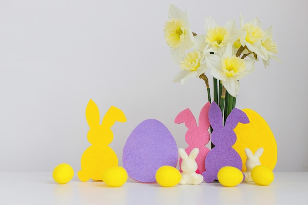 Fröhliche Ostern Bunte Osterhasen, Eier und Narzissen auf weißem Hintergrund mit Platz für Text