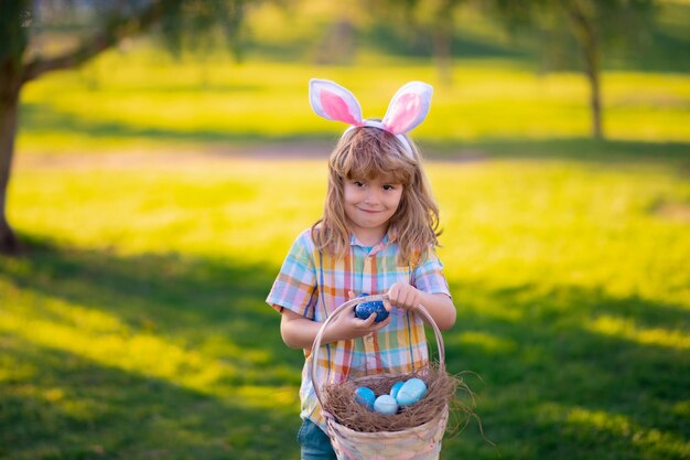 Fröhliche Ostern für Kinder Kinderjunge jagt Ostereier Nettes Kind im Kaninchenkostüm mit Hasenohren, die Ostern im Park haben Kinder jagen Ostereier