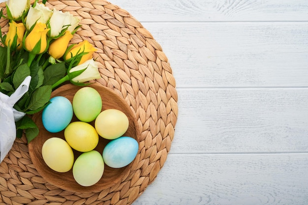 Fröhliche Ostern Ostereier auf rustikalem Tisch mit weißen und gelben Rosen Natürlich gefärbte bunte Eier in Holzplatte und Frühlingsblumen im rustikalen Raum Getöntes Bild Osterhintergrund mit Kopierbereich