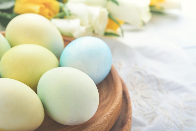 Fröhliche Ostern Ostereier auf rustikalem Tisch mit weißen und gelben Rosen Natürlich gefärbte bunte Eier in Holzplatte und Frühlingsblumen im rustikalen Raum Getöntes Bild Osterhintergrund mit Kopierbereich